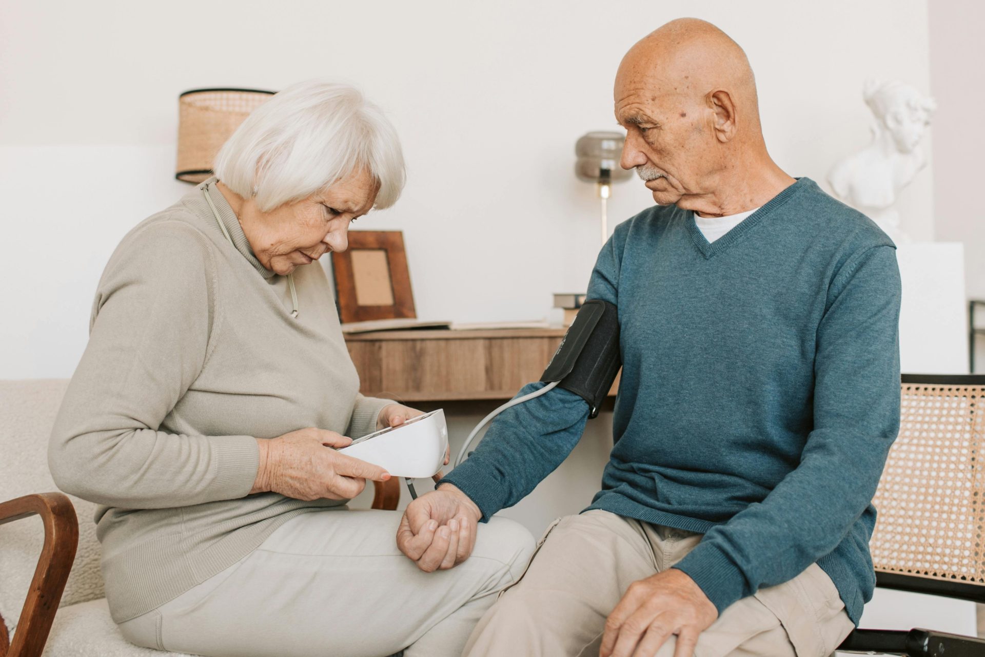 An elderly couple measuring blood pressure with a sphygmomanometer indoors.