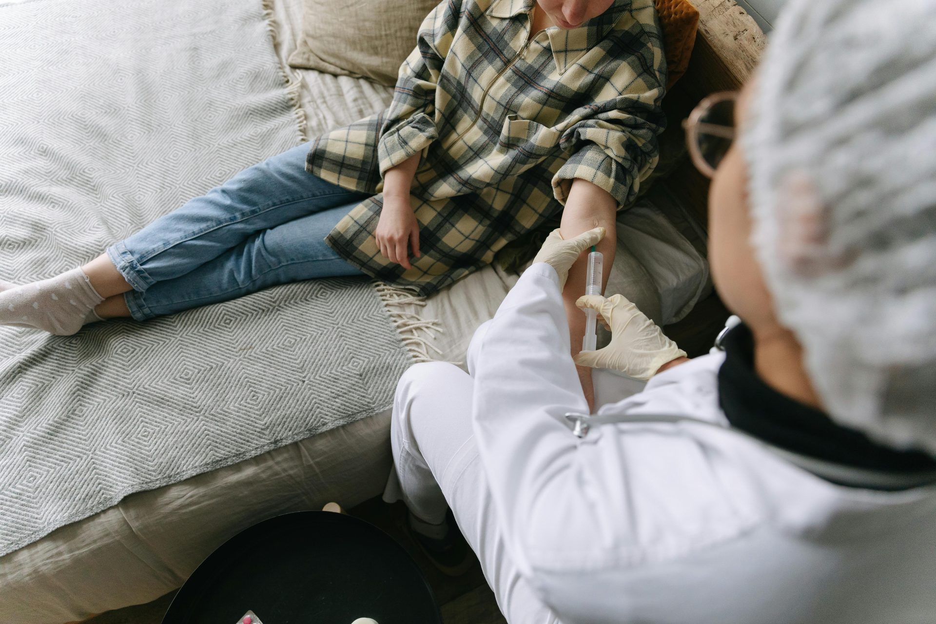 A healthcare professional carefully administers an injection to a patient sitting on a sofa in a cozy room.