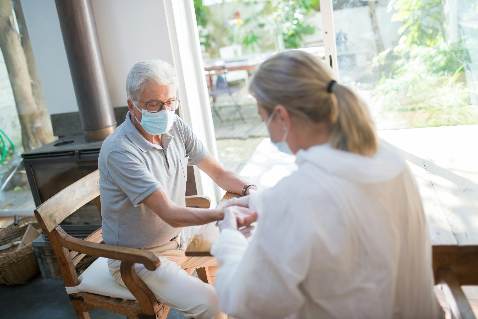 A healthcare worker examining a senior man at home with face masks during the pandemic.