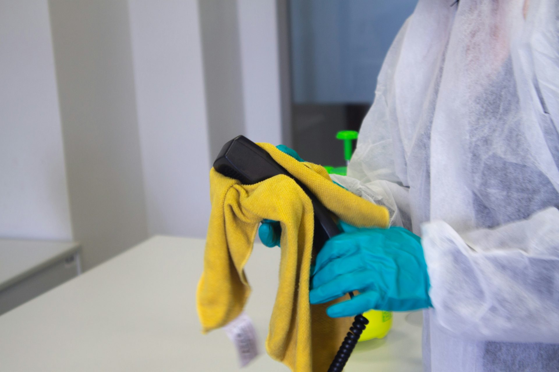 Worker in protective gear sanitizing office telephone