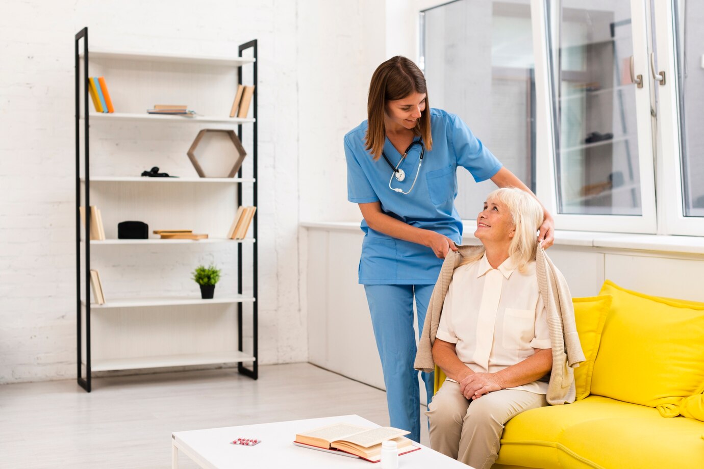 Nurse putting a coat on smiling elderly woman